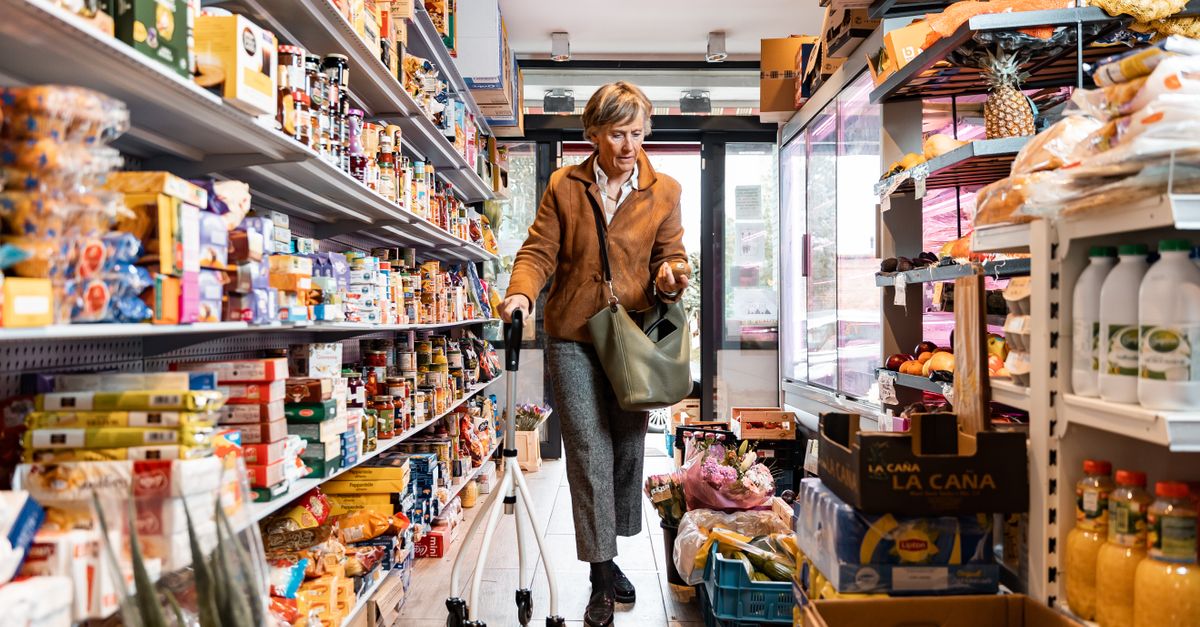 A senior woman using a rollator while shopping in a grocery store aisle.