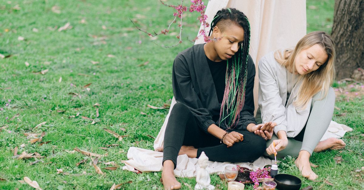 Two women meditating outdoors with yoga accessories, embracing relaxation and diversity.