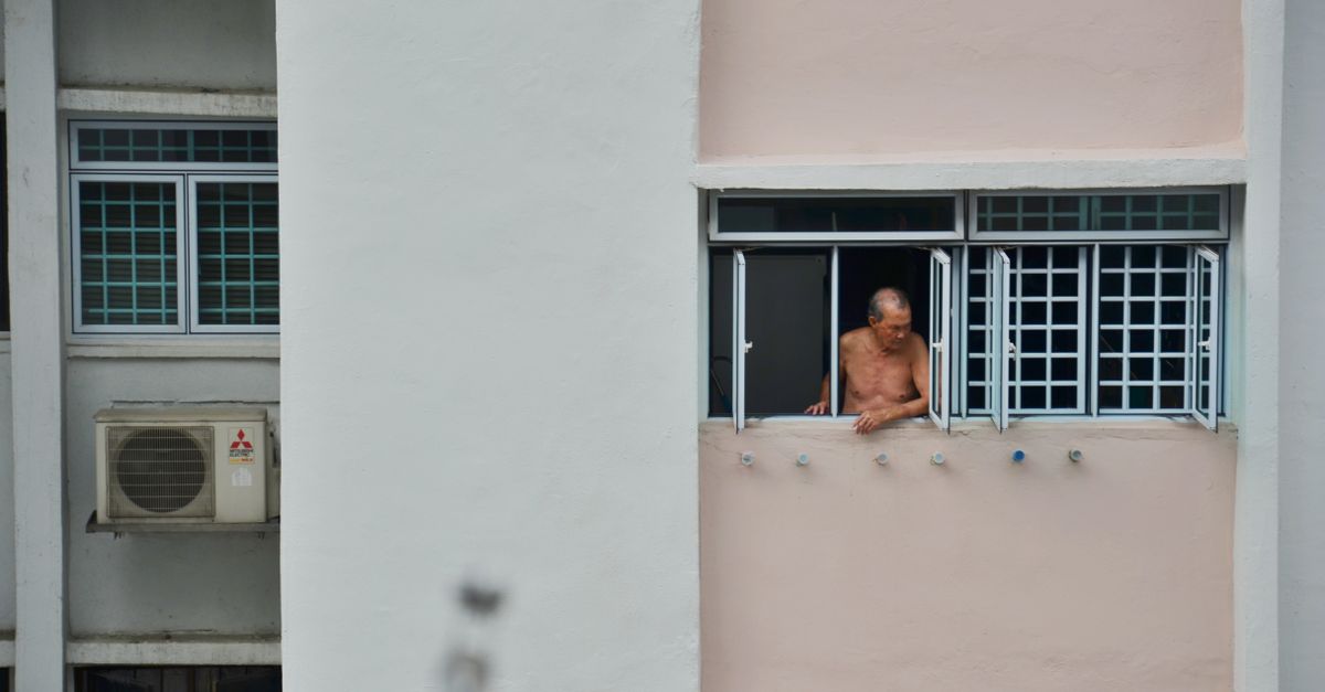 Elderly man gazing from an urban high-rise window, evoking solitude.