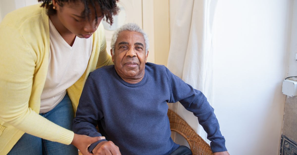 A woman assists an elderly man indoors, focusing on care and support.