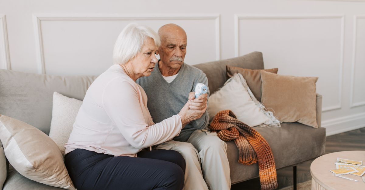 Elderly couple checking temperature with digital thermometer, highlighting health care at home.