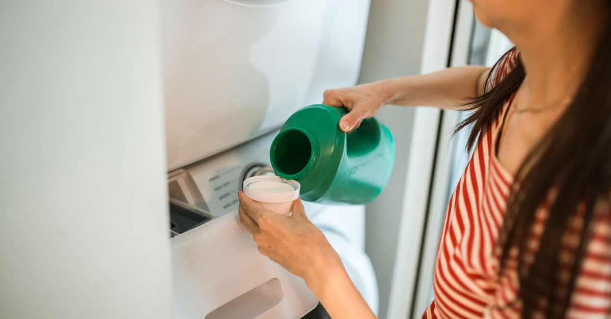A woman pours detergent into a washing machine in a home laundry room.