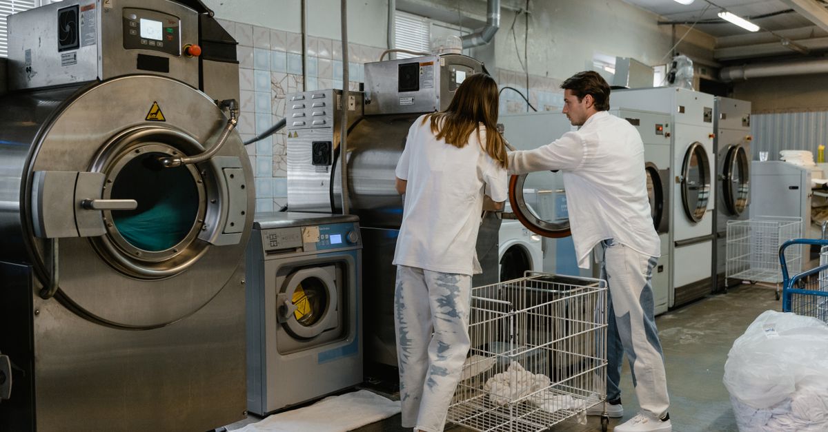 Two adults working in an industrial laundry facility with large machines.