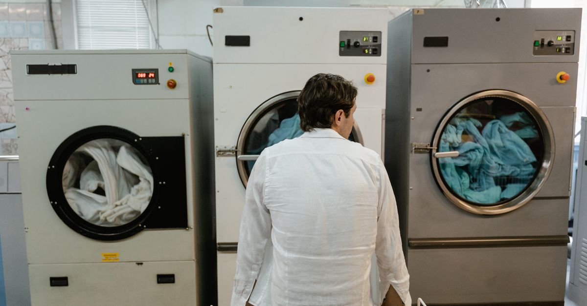 A man uses commercial washing machines at an indoor laundromat.