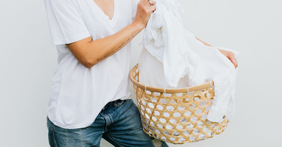 A woman holding white laundry in a stylish bamboo basket against a clean white background.