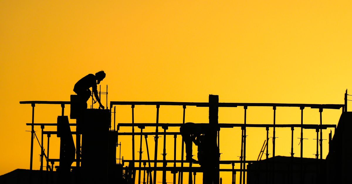 Silhouette of construction workers on a building site during a vibrant sunset, symbolizing progress and hard work.