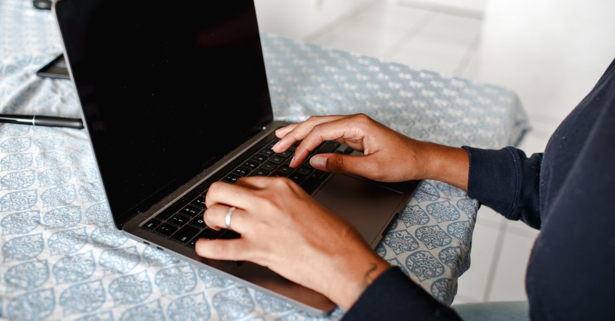 Close-up of hands typing on a laptop indoors on a patterned tablecloth.