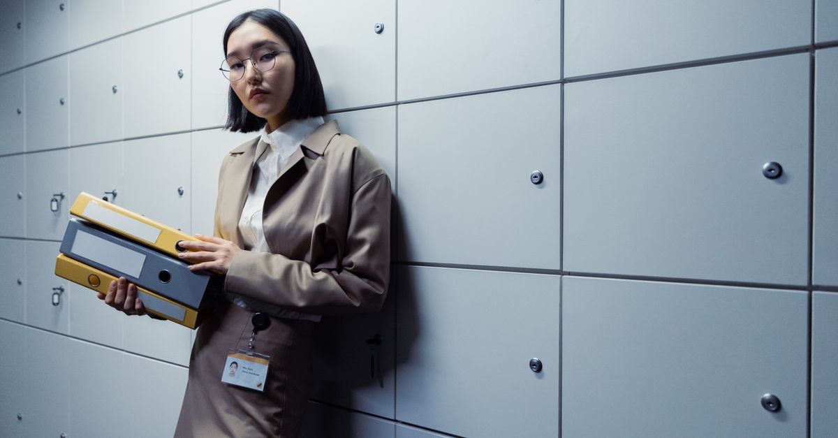 Businesswoman in office attire standing with documents, appearing poised in a modern office setting.