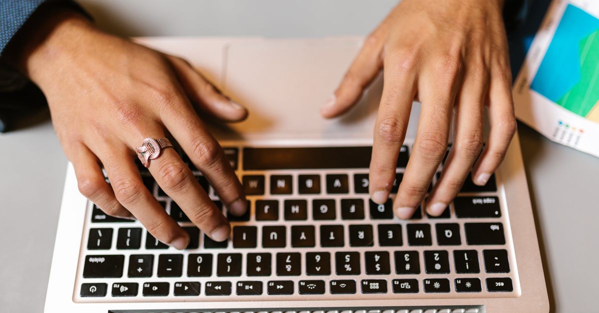Hands typing on a laptop with a ring, emphasizing technology and work.
