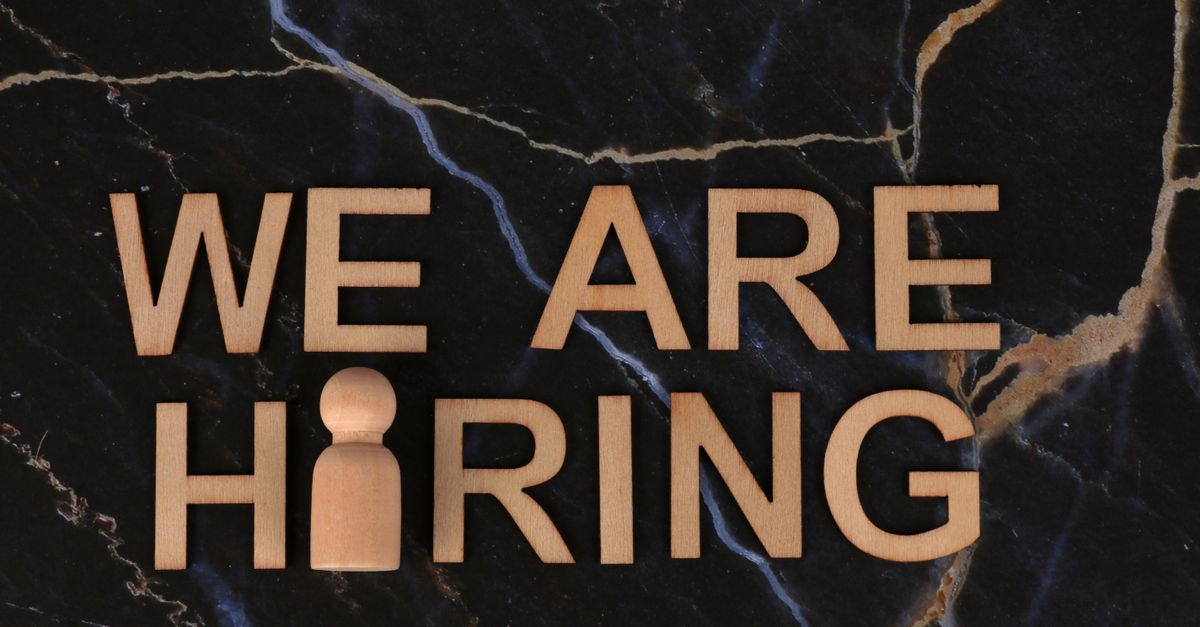 Wooden letters spell 'We Are Hiring' on dark marble surface.