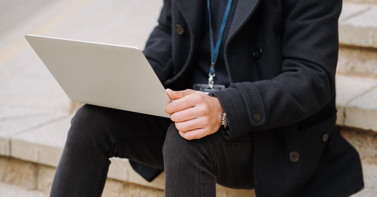 Crop anonymous male office employee in formal apparel with netbook working on project on street staircase