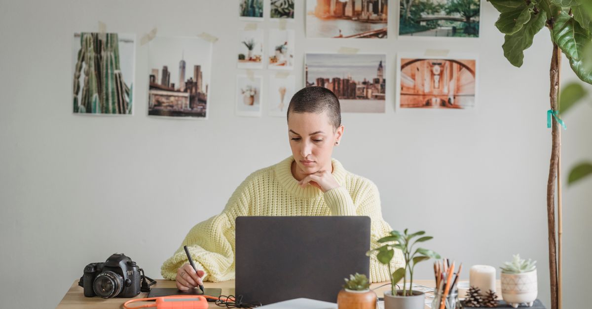 Concentrated woman using graphic tablet while sitting at table with laptop in daylight