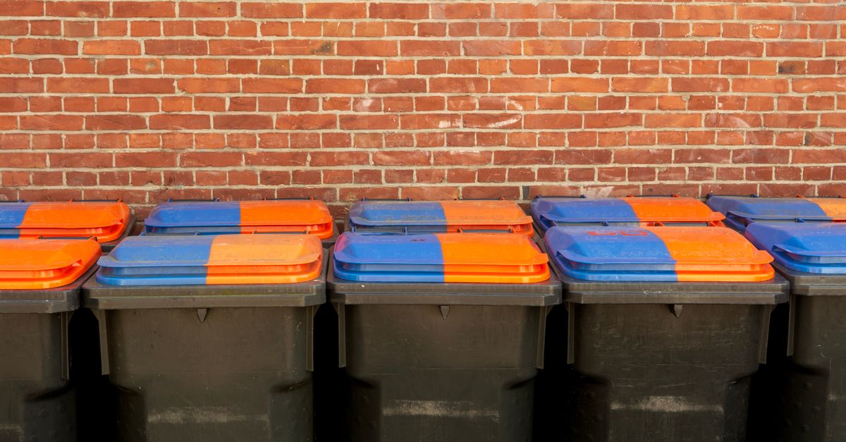 Row of recycling bins with vibrant lids in front of a brick wall for urban waste management.