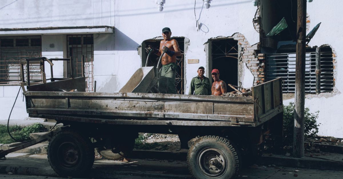 Workers loading debris onto a truck at an urban construction site. Manual labor in progress.