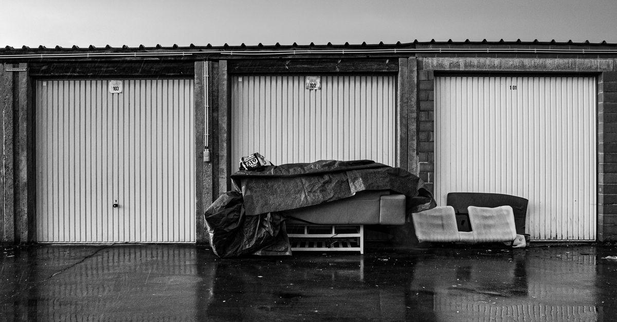 Monochrome view of closed storage units with covered furniture outdoors on a rainy day.