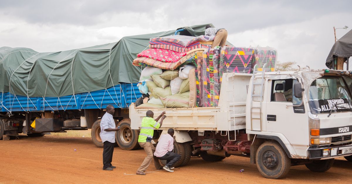 People loading supplies onto a truck in a rural area under cloudy skies.