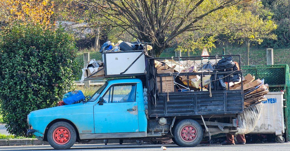 Side view of a vintage blue truck loaded with recyclable waste on a sunny day.