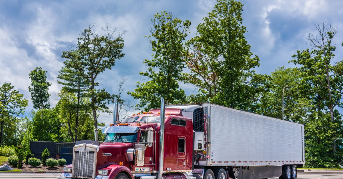 A striking red semi truck parked in a lush scenic area, showcasing modern transportation technology.