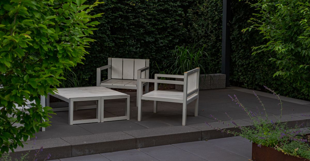 A serene outdoor patio featuring minimalist wooden furniture in a lush garden setting.