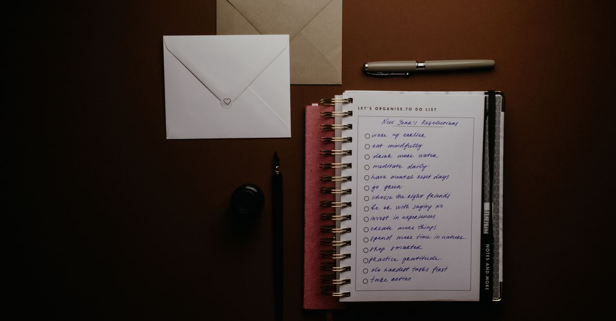 Overhead view of a to-do list notebook with New Year's resolutions, pens, and envelopes on a desk.