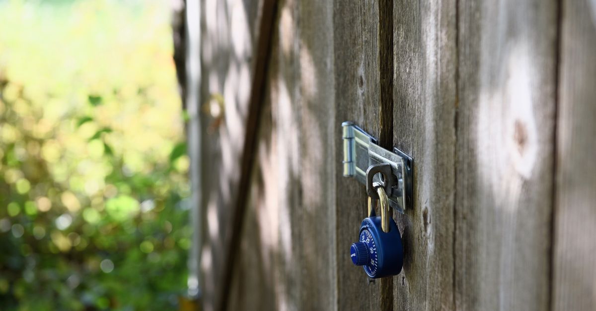 A blue padlock secures a wooden gate outdoors with sunlight filtering through.