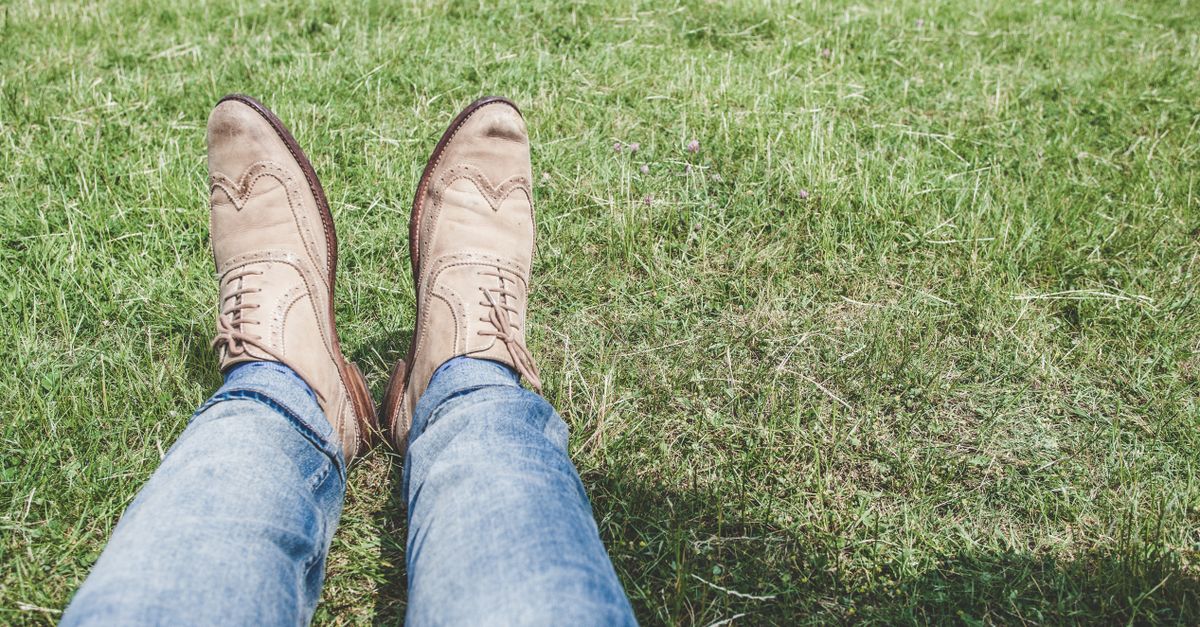 Casual view of shoes and denim jeans on a vibrant green lawn, suggesting relaxation.