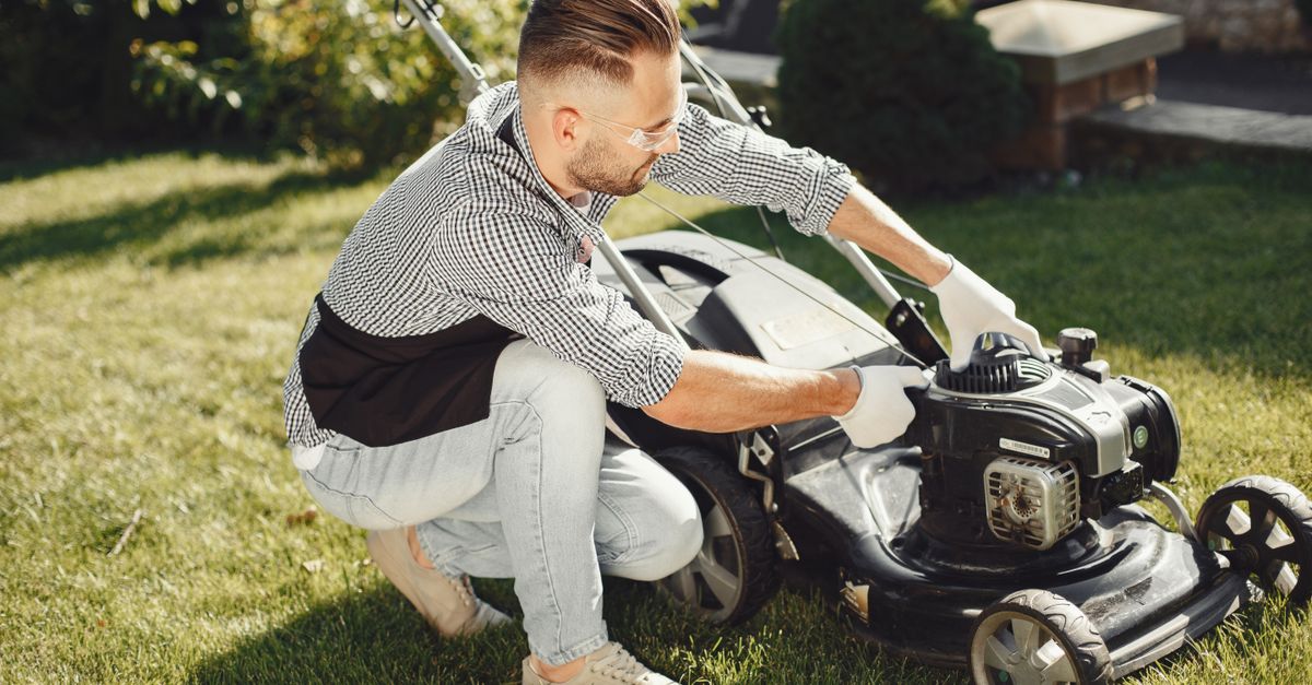 Man preparing lawn mower for garden work on a sunny day outdoors.