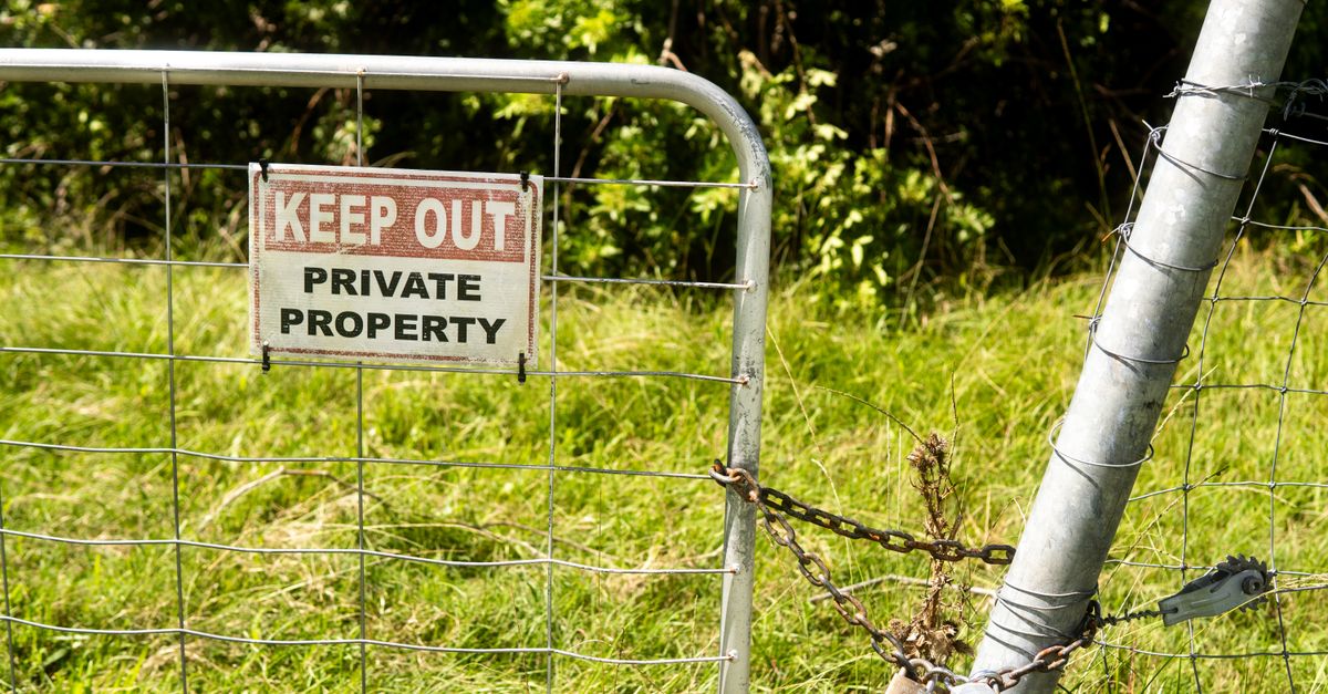 Metal fence with 'Keep Out Private Property' sign in a grassy outdoor setting.
