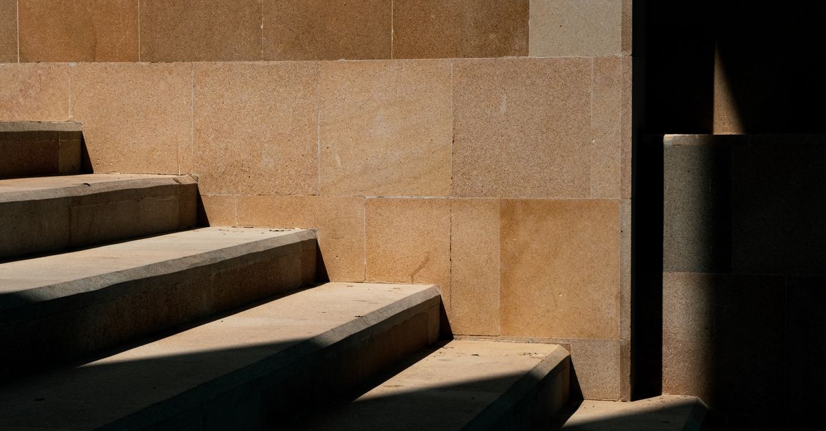 Close-up of shadows cast on stone stairs and a tile wall in an urban setting.