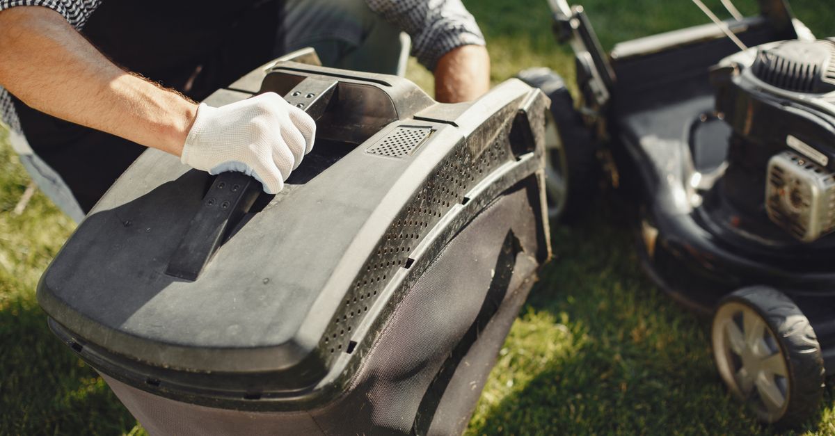 An adult man replacing a lawn mower bag on a sunny day in the yard.