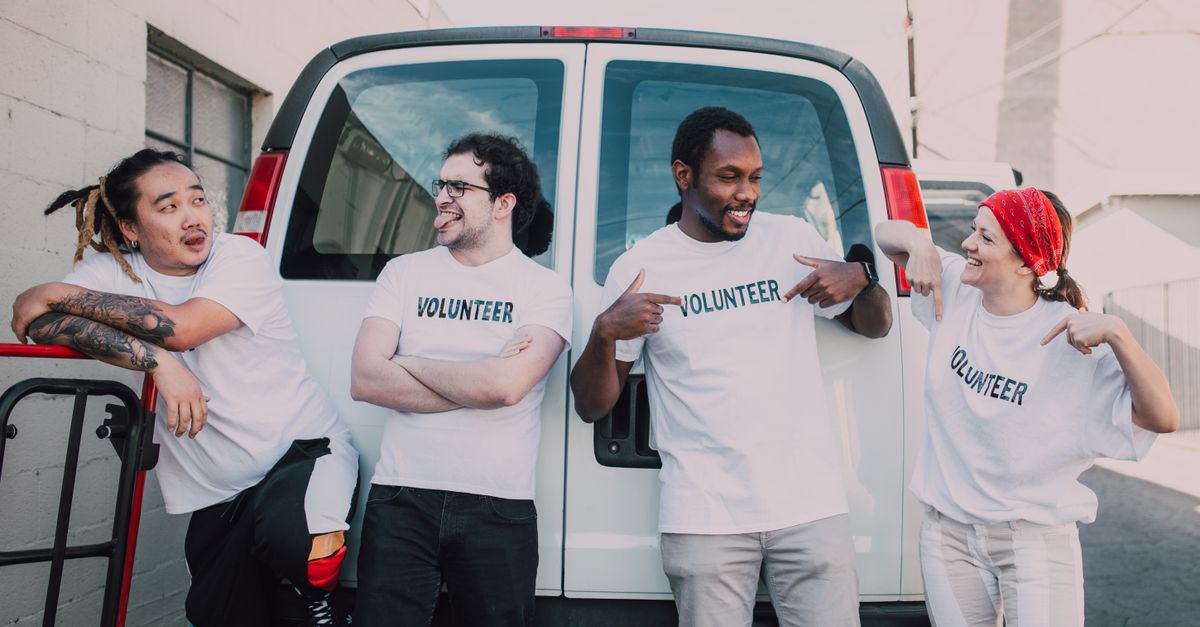 A diverse group of volunteers standing outside a van, smiling and socializing.