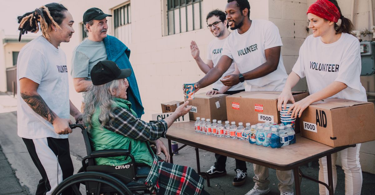 Volunteers distribute bottled water and supplies to diverse individuals in an outdoor setting, showcasing community support.