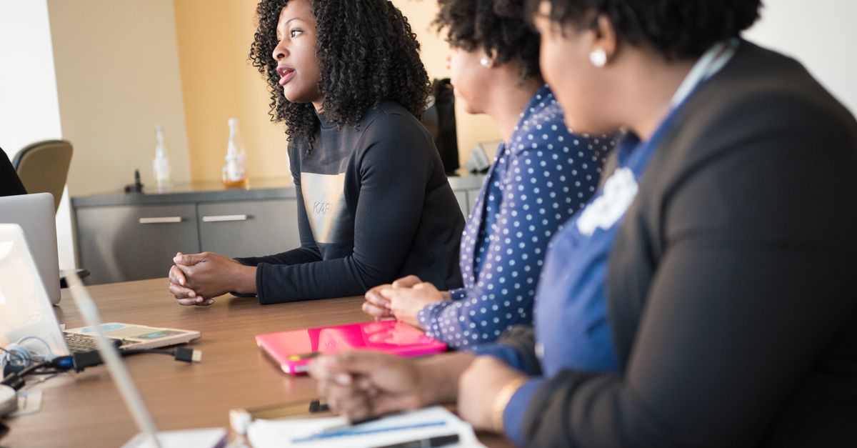 A group of women engaged in a professional meeting, collaborating in a modern office setting with laptops and documents.