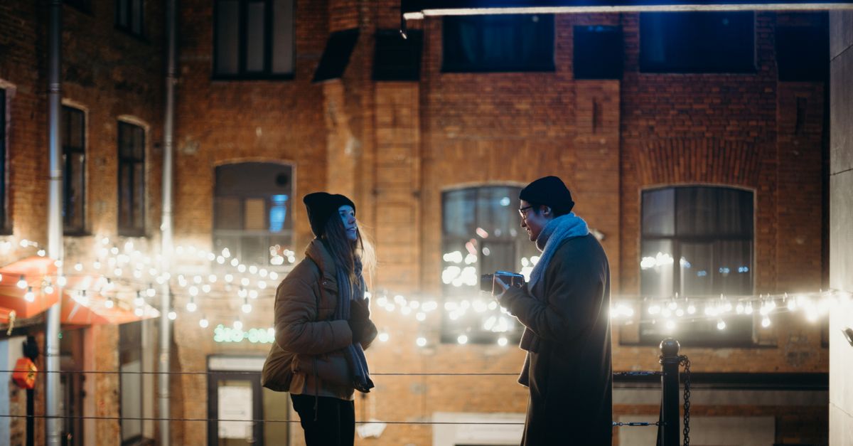 Two people conversing outdoors in a cozy winter setting with festive lights.