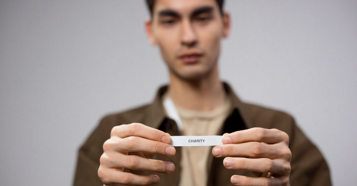 A man holds a note reading 'charity,' with the focus on his hands, expressing a charitable theme.