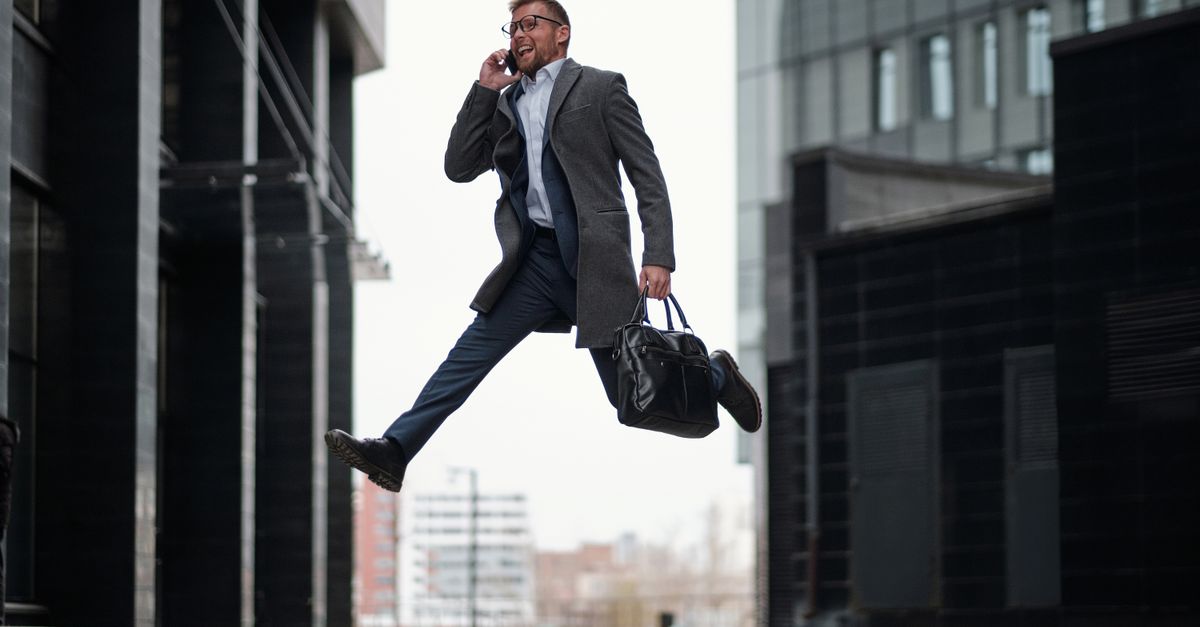 Dynamic businessman jumping while talking on phone in a modern cityscape.