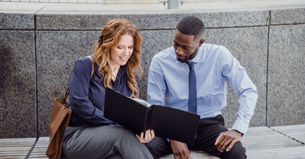 Two colleagues discussing a document while seated on an outdoor bench, showcasing teamwork.