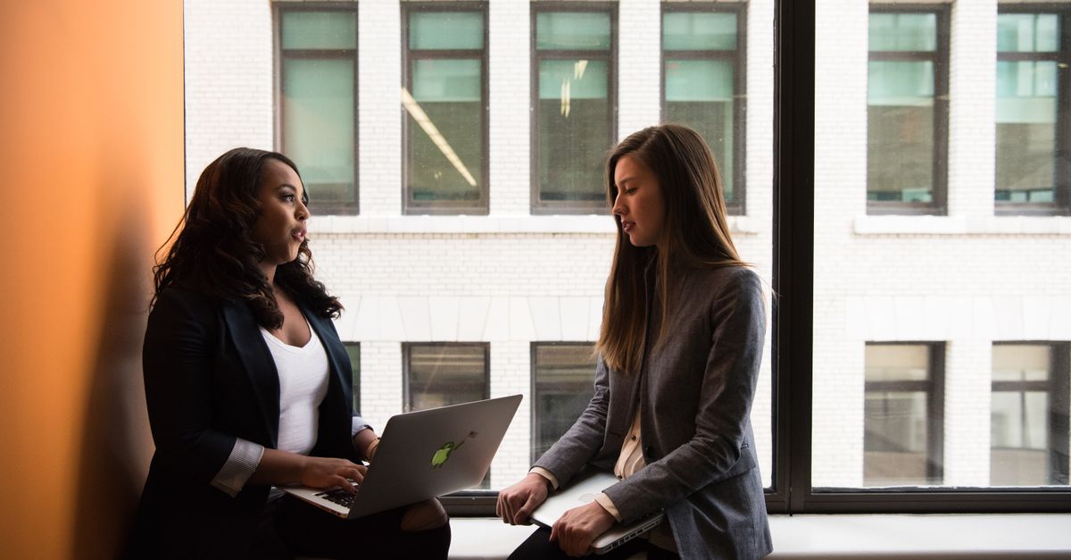 Two women having a business discussion in an office setting, using a laptop.