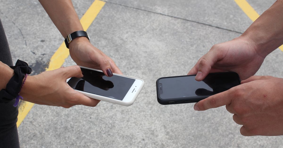 Two people exchanging or comparing smartphones in an outdoor setting, focusing on hands and technology.