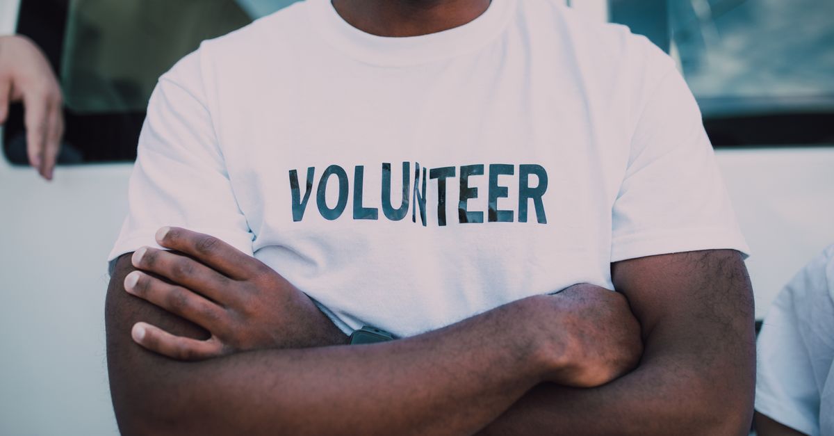 A close-up of a person wearing a volunteer shirt with arms crossed, promoting community service.