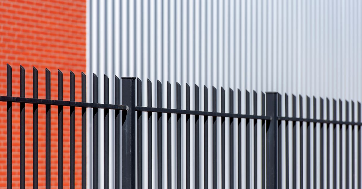 Black metal fence contrasts with red brick and corrugated metal backdrop, offering a sleek industrial look.