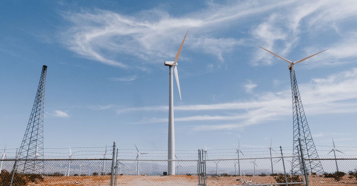 Desert landscape with wind turbines and transmission towers under a clear sky.