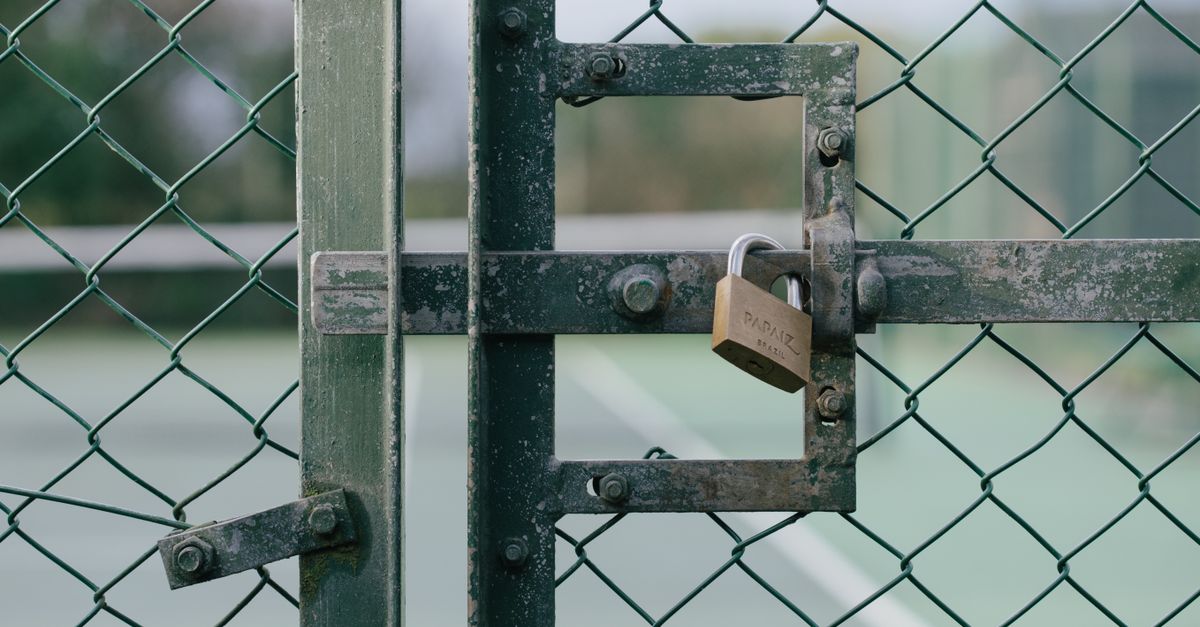 Close-up of a locked gate with chain link fence at a tennis court outdoors.