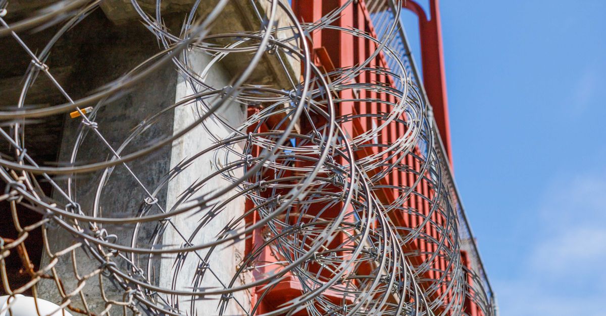 Close-up of barbed wire on an industrial fence against a blue sky.