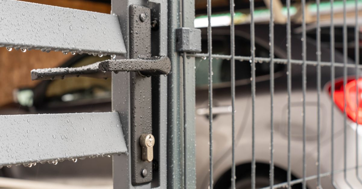 Detailed view of a wet metal gate with raindrops and a parked car in the background.