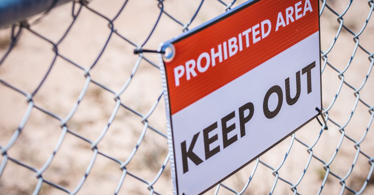 Close-up of a 'Prohibited Area' and 'Keep Out' sign on a chain link fence.