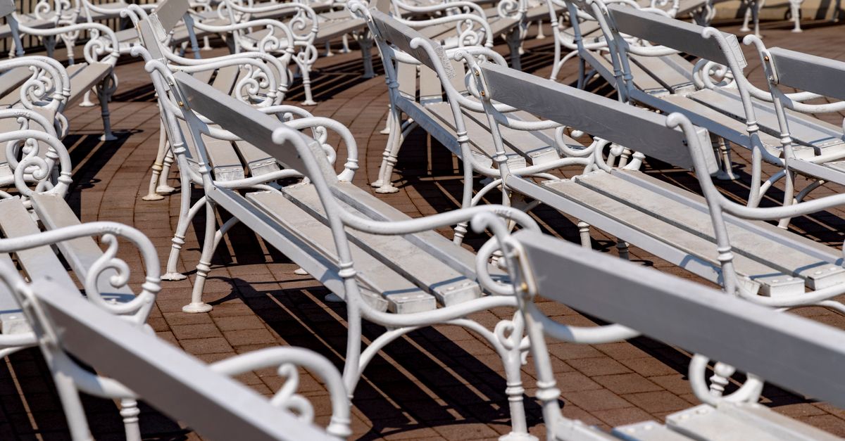 Elegant white metal benches lined up in a sunlit outdoor plaza.