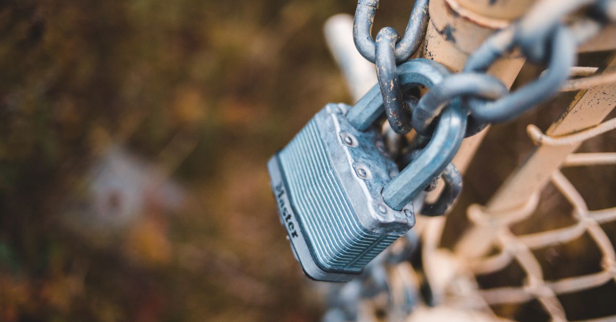 From above of small metal lock on chain attached to shabby net mesh fence in autumn park