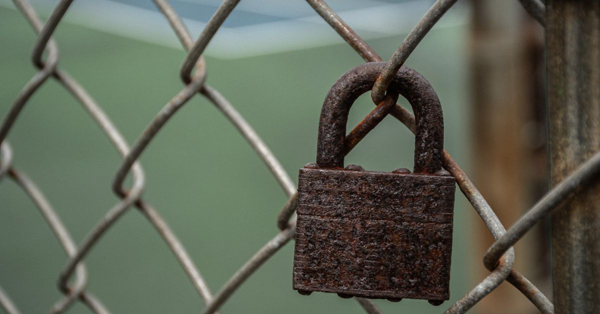 A highly detailed image of a rusted padlock hanging on a chain-link fence.