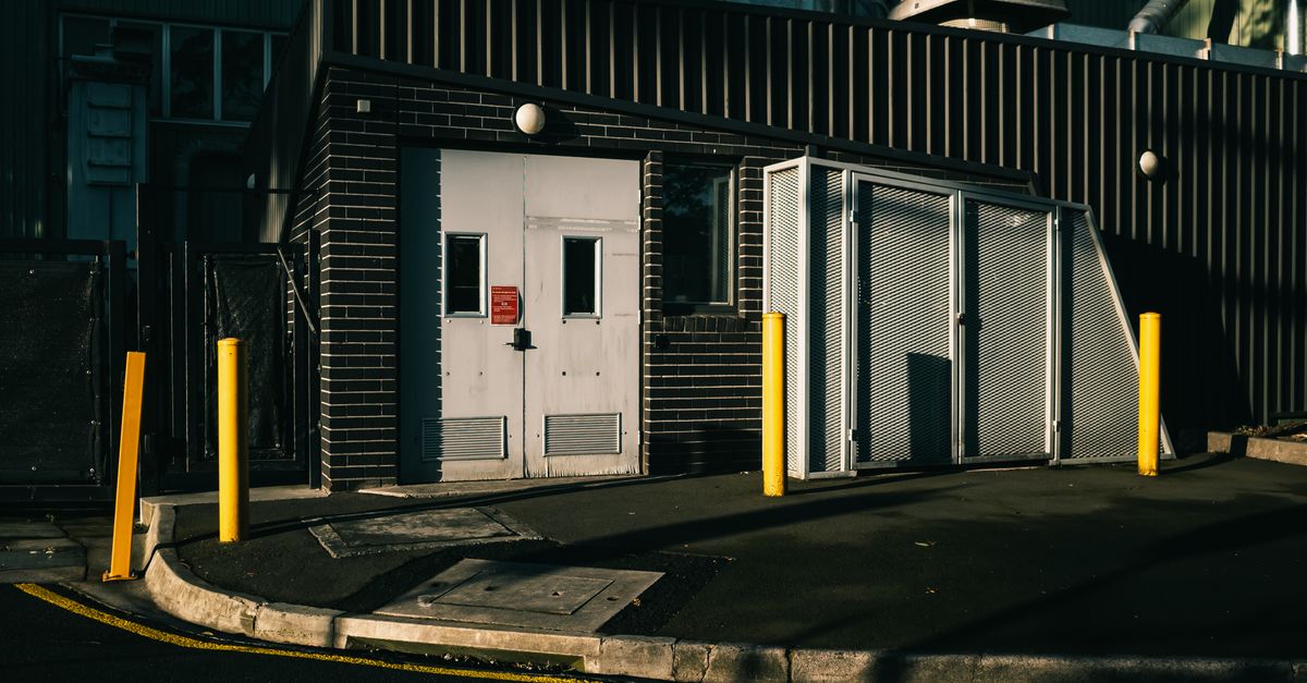 Exterior view of an industrial building with metal doors and bollards.